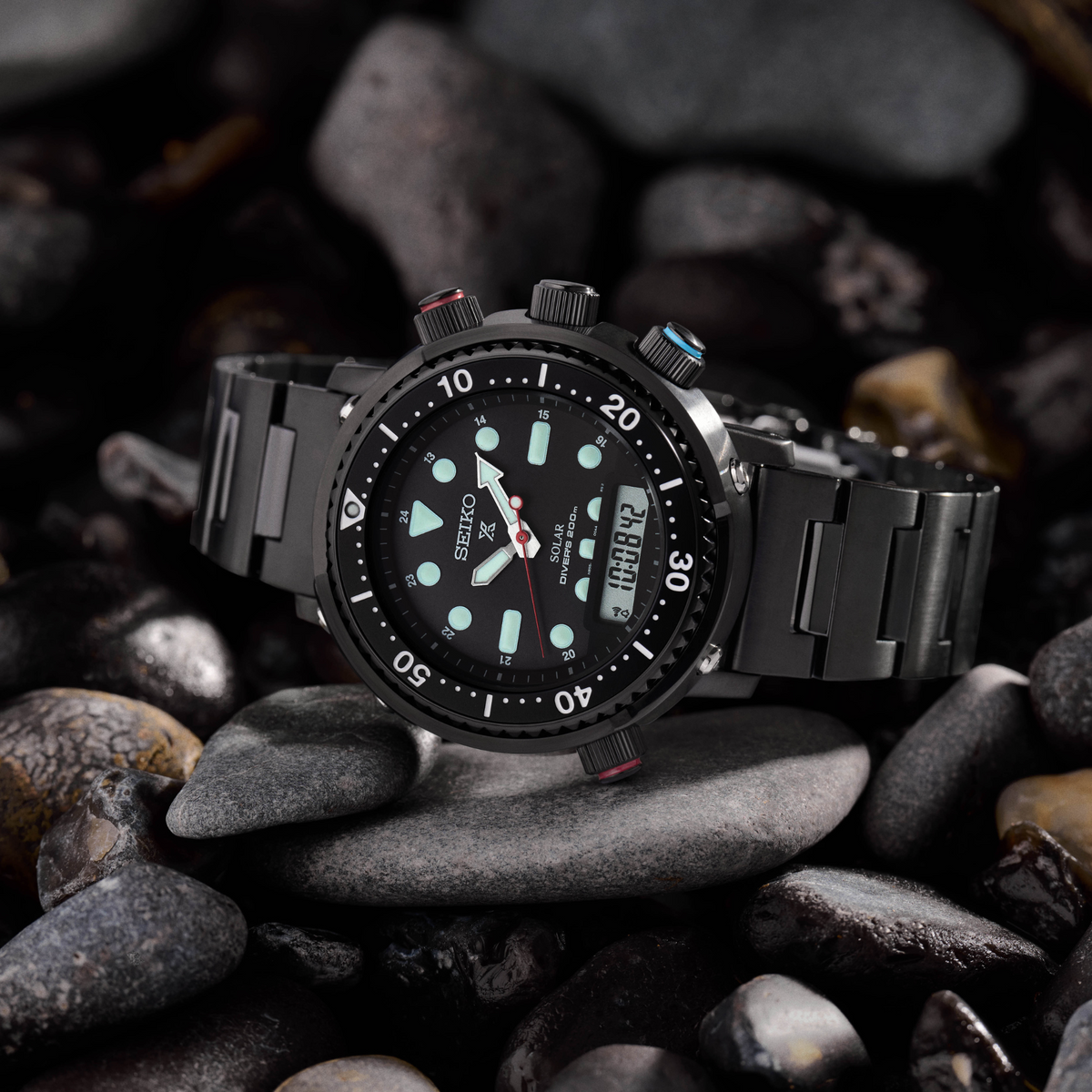 Black solar diver watch on dark rocks, black dial with teal markers and red seconds