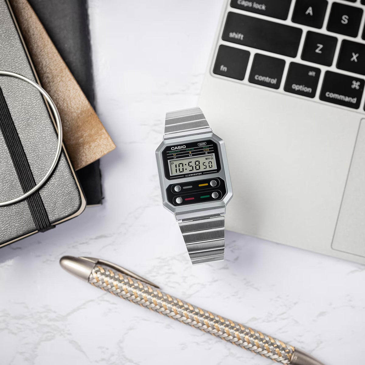 Casio digital watch with silver steel bracelet on desk, rectangular LCD display