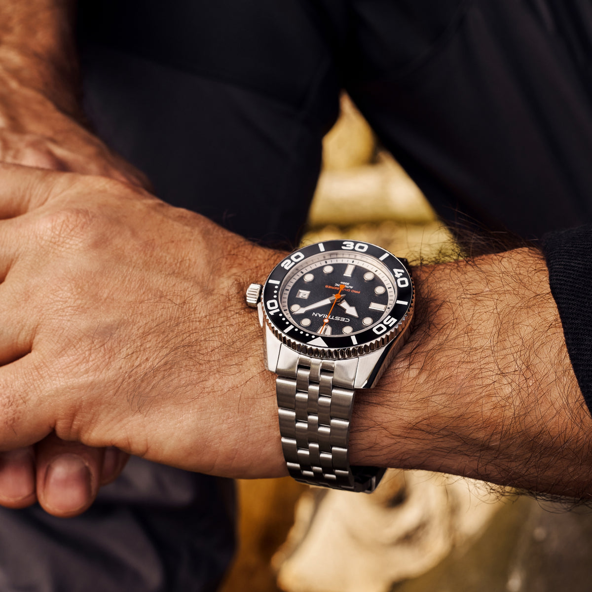 Close-up of men's black dive watch dial with bezel numerals and silver bracelet