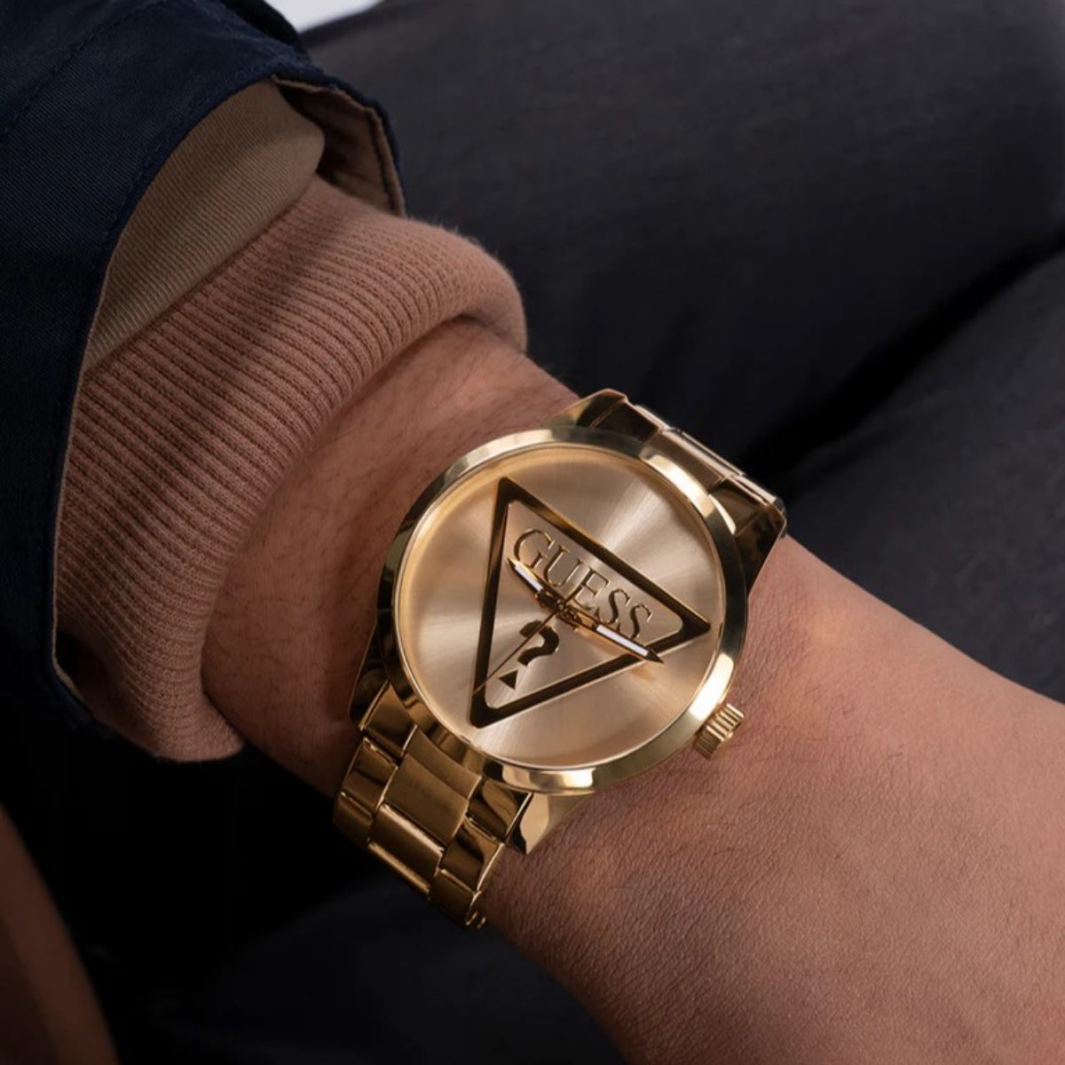 Gold analog men's watch on wrist, GUESS triangular dial with logo