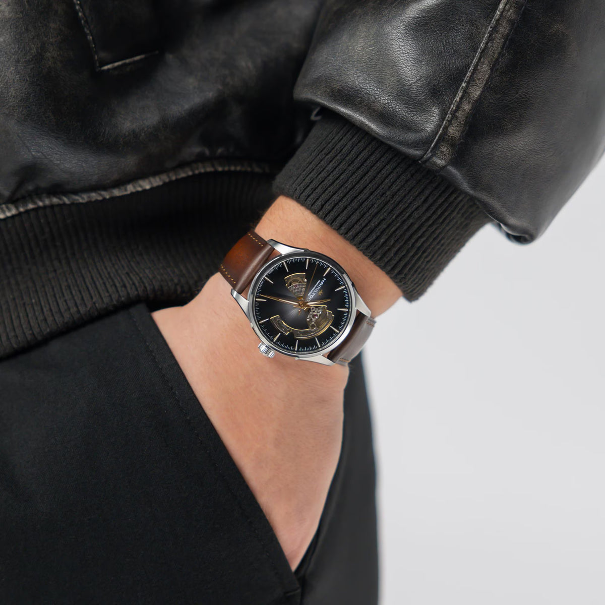 Hamilton Jazzmaster H32705501 automatic watch wrist shot styled with a leather jacket, showing an open heart brown dial