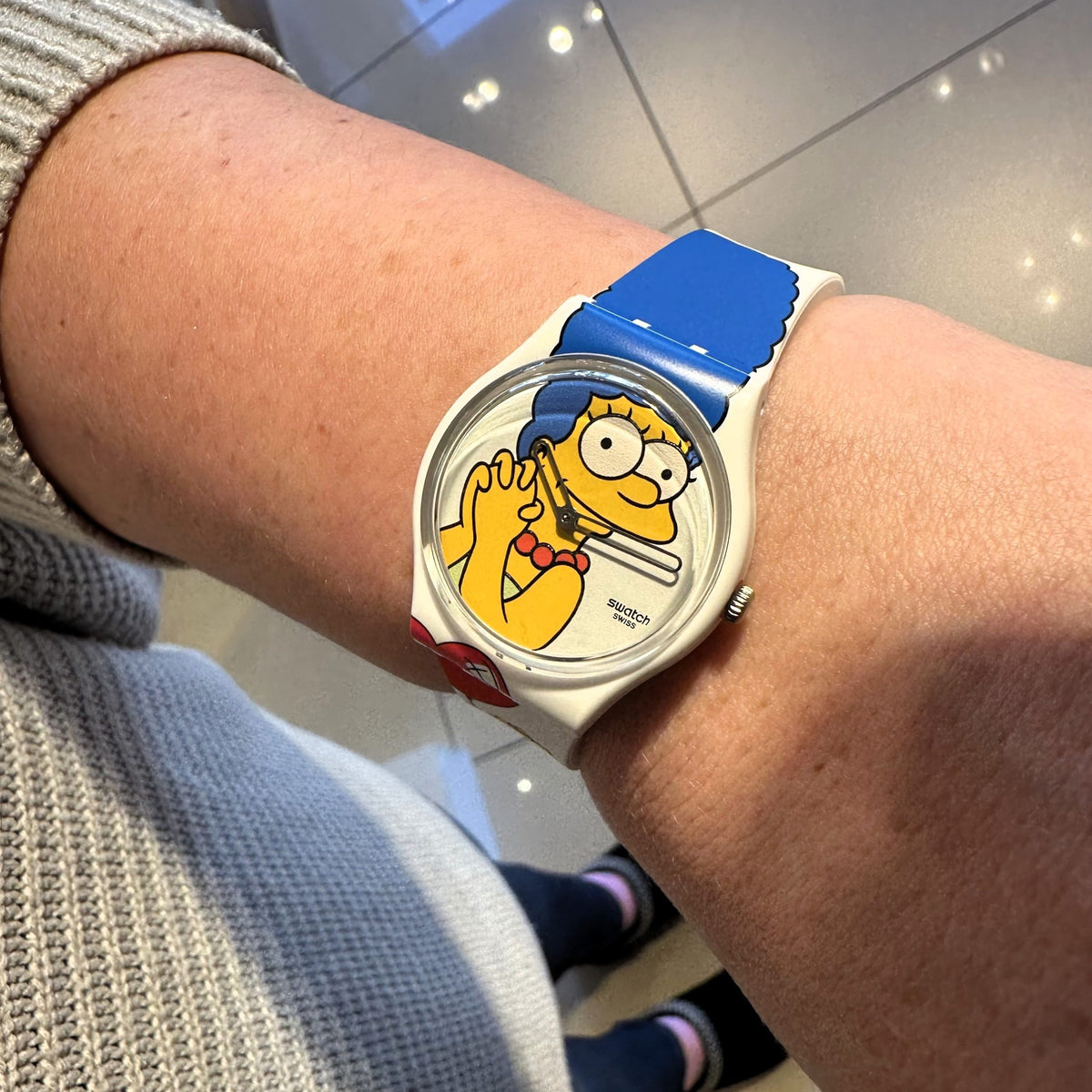 Swatch ladies watch on wrist with white strap and blue top graphic, round Homer face
