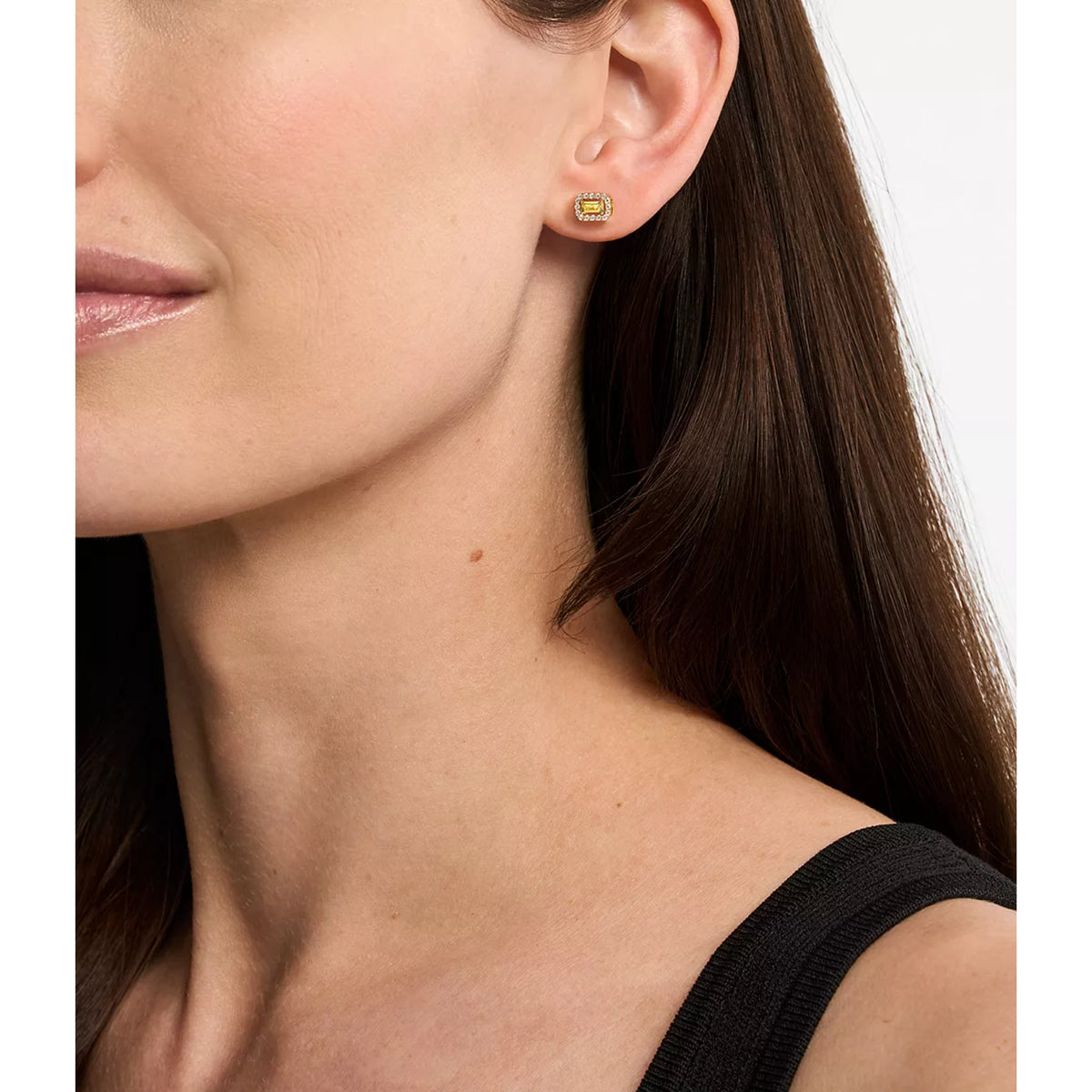 Gold-plated emerald-cut stud earrings with green center stones shown on a pierced ear