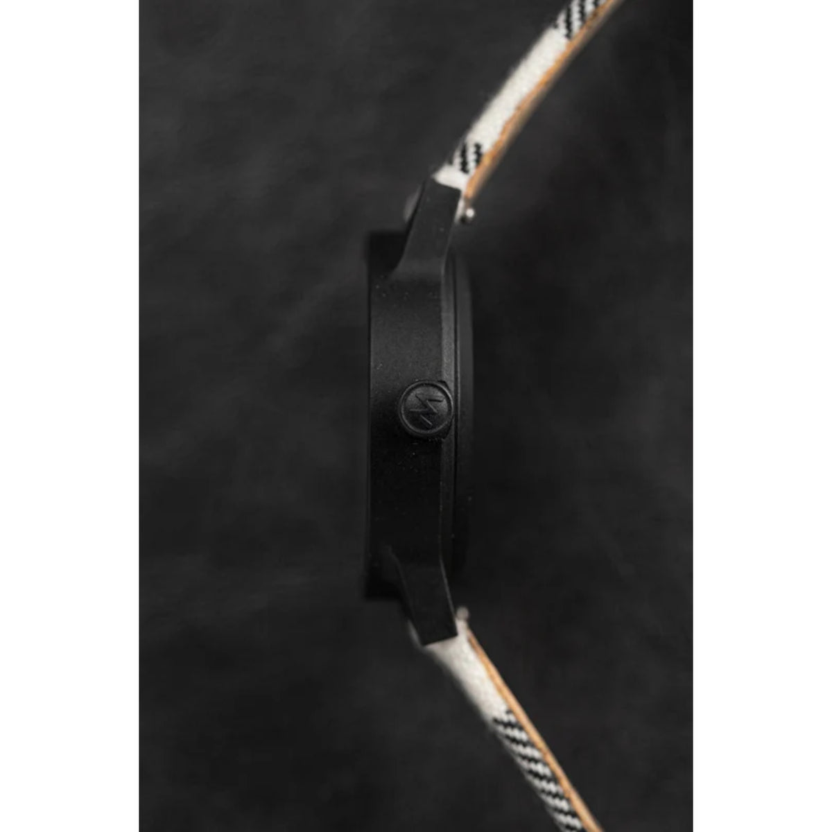 Quartz wristwatch side profile with black case, black strap, and tan patterned edge