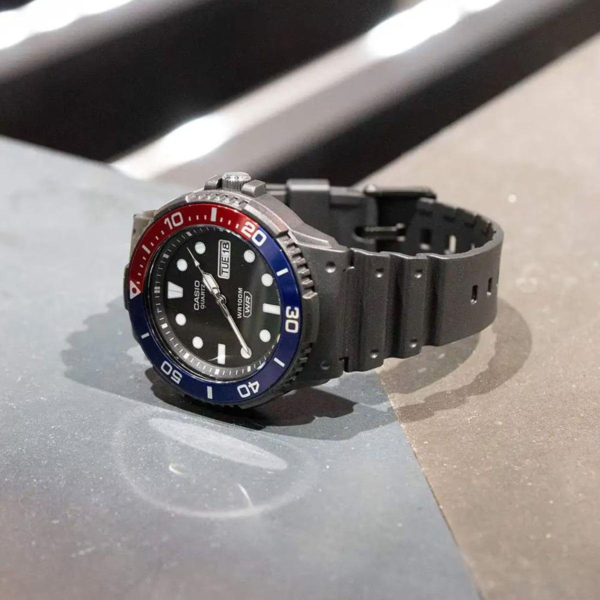 Side angle shot of the Casio Sport Standard MRW-230H-1E2VEF black dial watch with a durable resin band lying on a flat surface