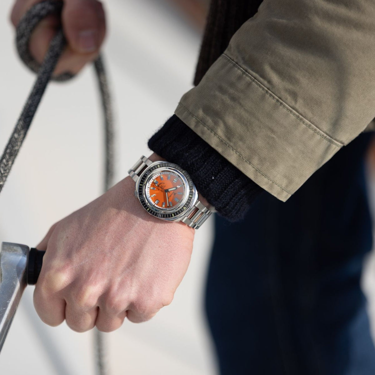 Men's steel automatic watch on wrist with orange dial and metal bracelet