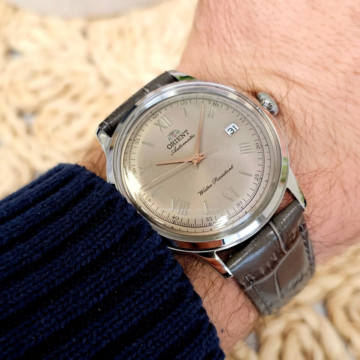 Men's automatic watch with beige dial, silver case, and dark leather strap on wrist
