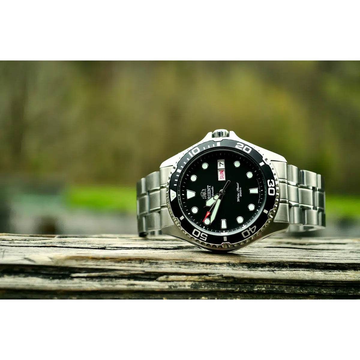 Men’s stainless automatic dive watch resting on wood with black dial and bezel