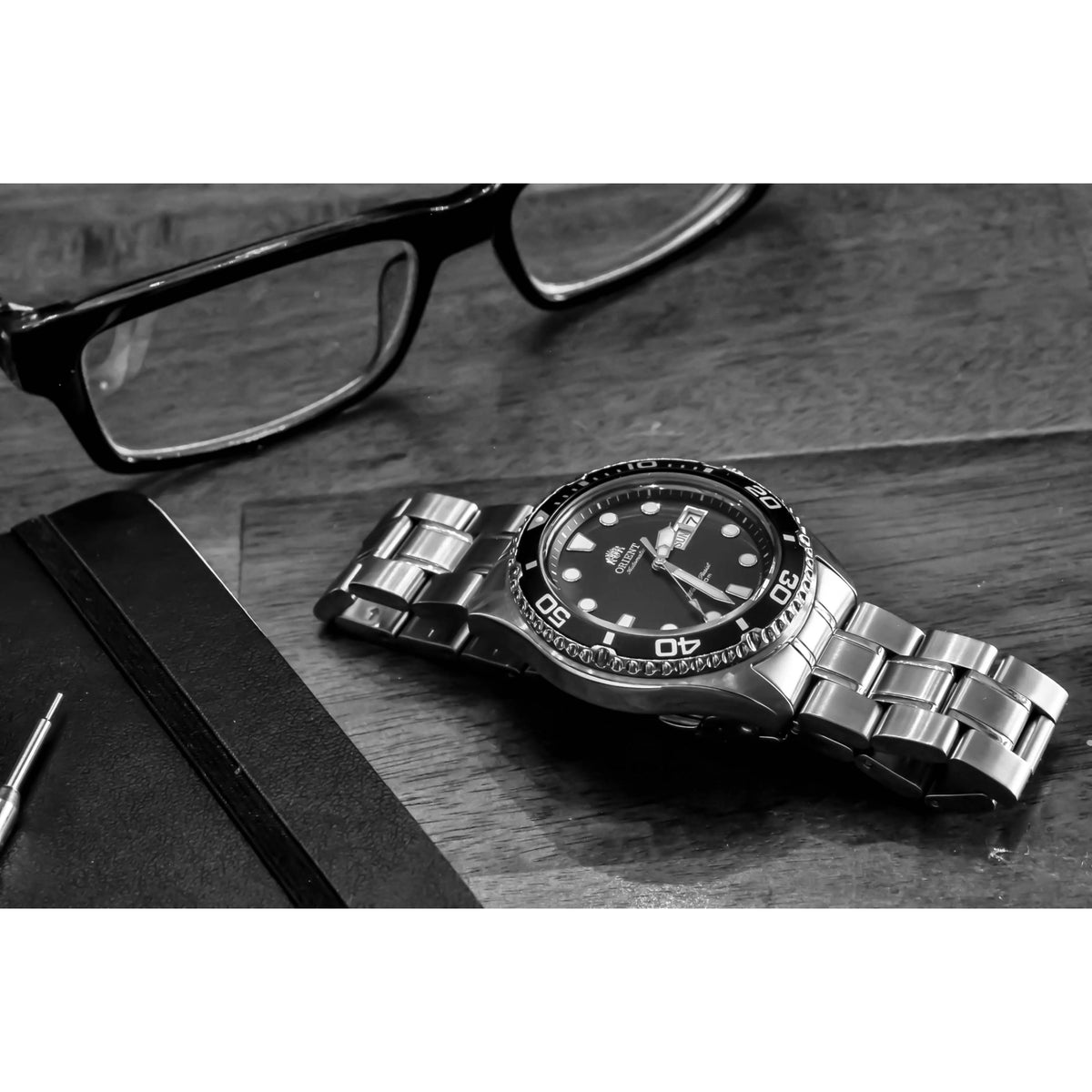 Men’s stainless steel dive watch with black dial on tabletop beside eyeglasses