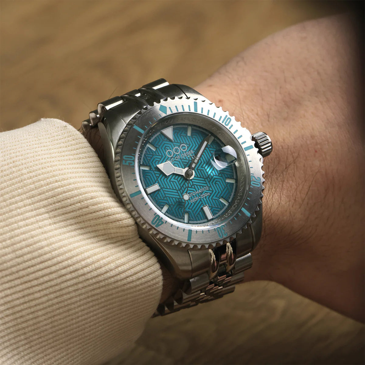 Men's dive watch with teal patterned dial and dark steel bracelet on a wrist.