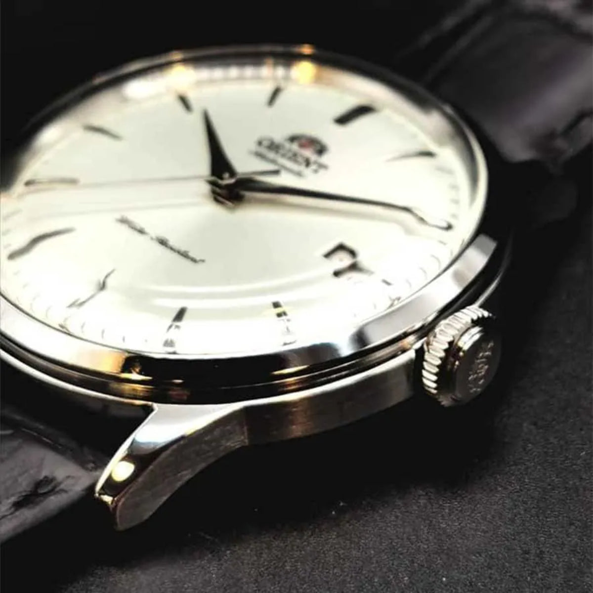 Close-up of automatic watch with white dial, black leather strap, silver hour markers