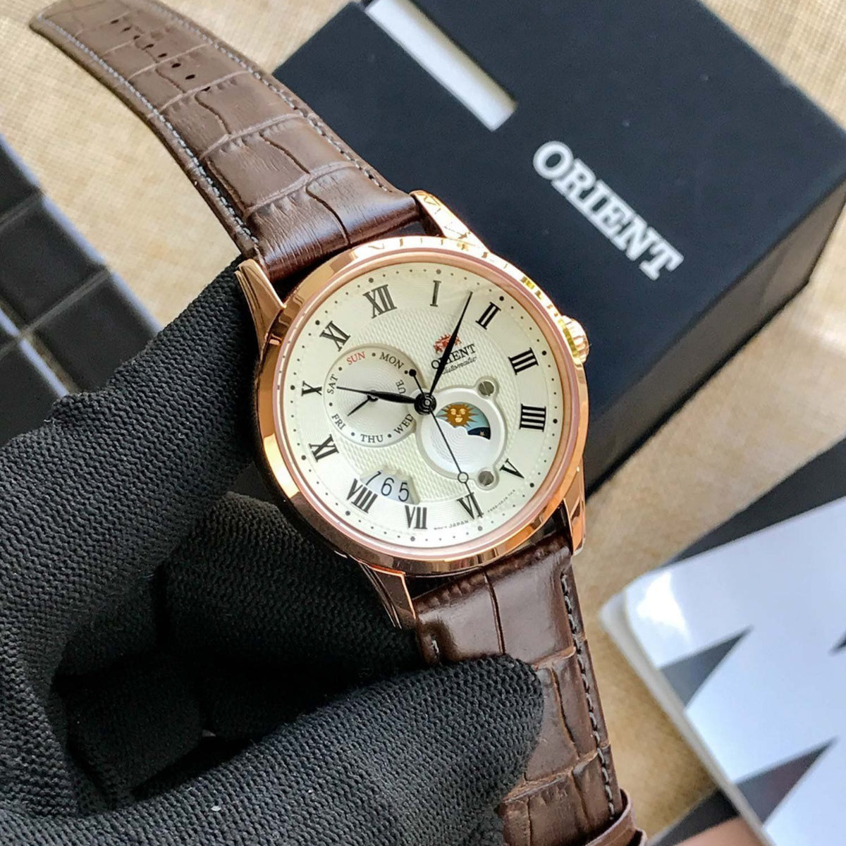 Angled view of Orient Bambino Sun & Moon RA-AK0007S30B mens watch highlighting rose gold-tone case and champagne dial