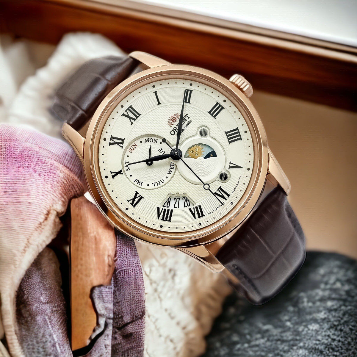Orient Bambino Sun & Moon RA-AK0007S30B mens automatic wristwatch with champagne dial resting on a soft fabric background