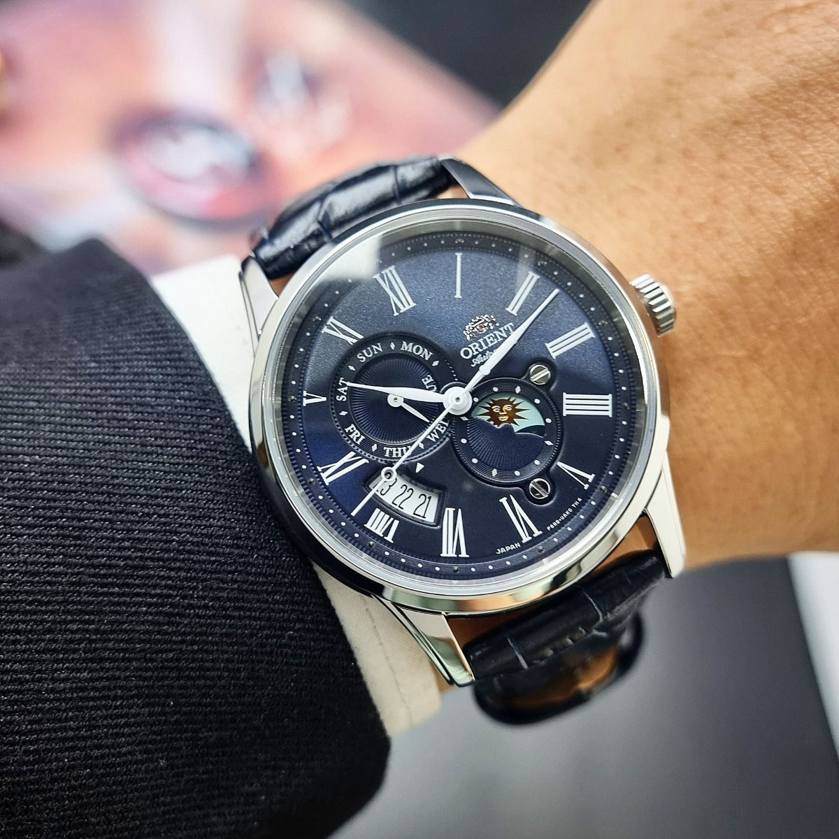 Orient Sun and Moon RA-AK0011D30B blue dial mens timepiece worn on wrist with suit sleeve