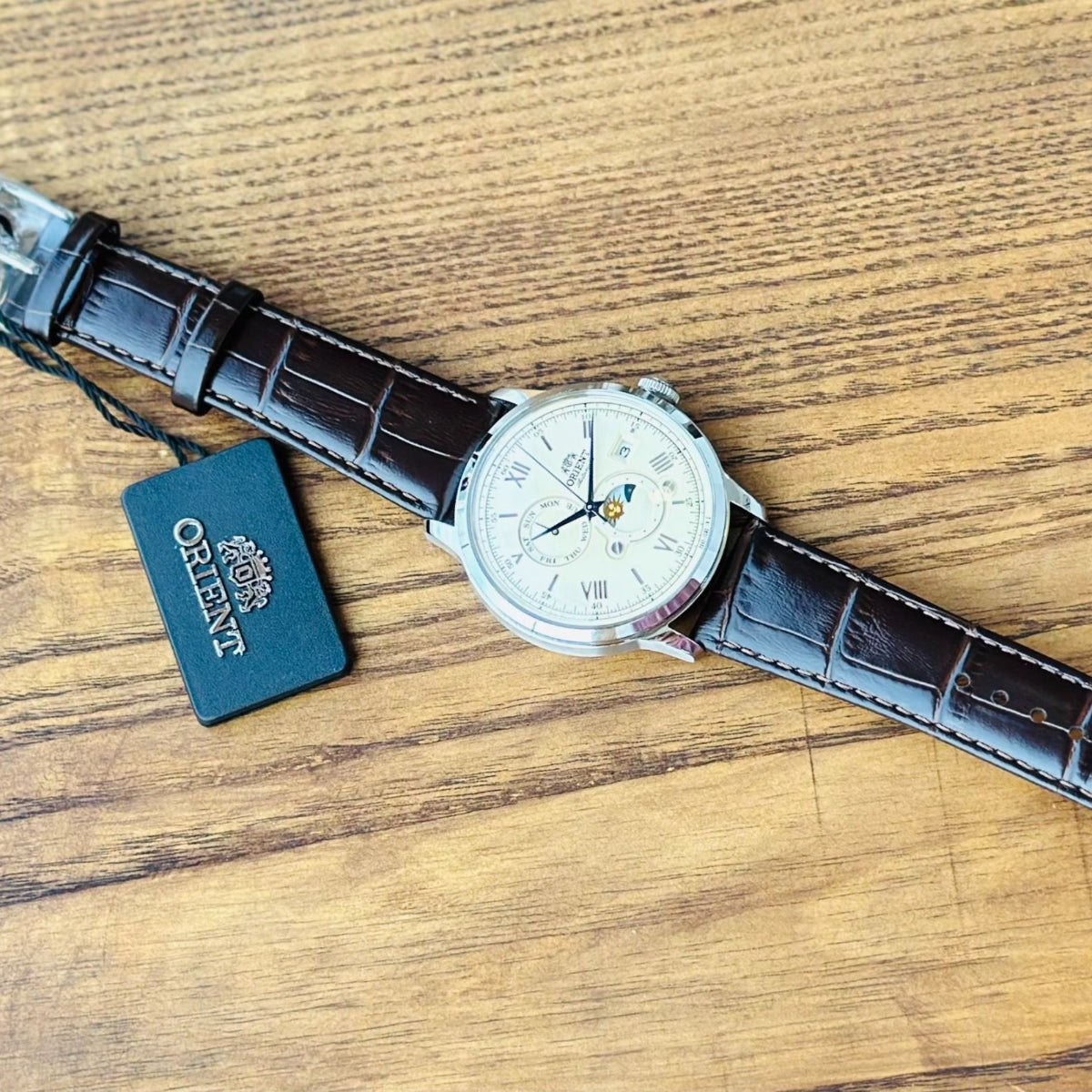 Orient Automatic Sun and Moon flat lay view with brand tag on wooden surface