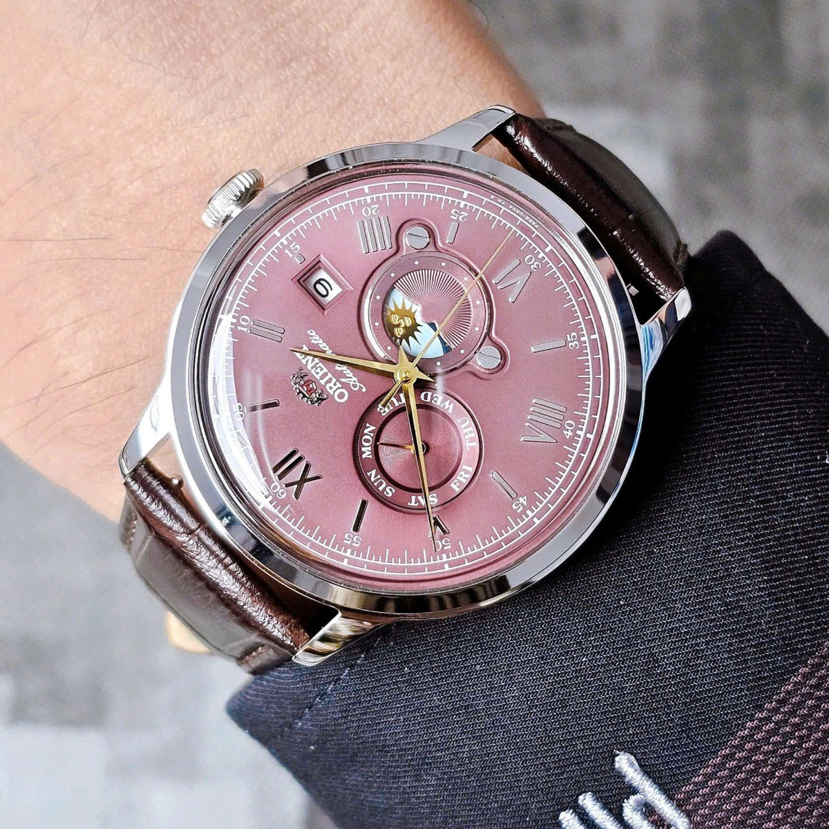 Orient Bambino Sun & Moon RA-AK0807R30B mens dress watch with a red dial worn on the wrist under a dark suit cuff