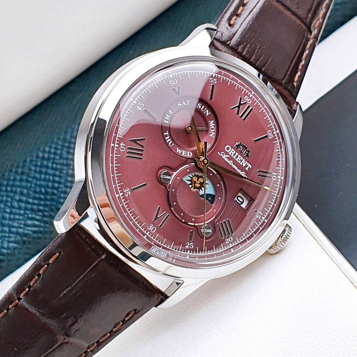 Macro view of Orient Bambino RA-AK0807R30B red dial with sun and moon sub-dials and Roman numerals