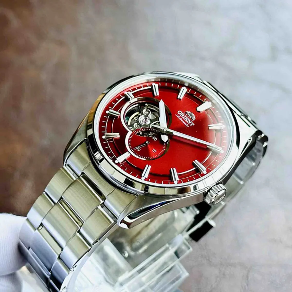 Men’s steel automatic watch with red dial and open-heart movement, angled close-up