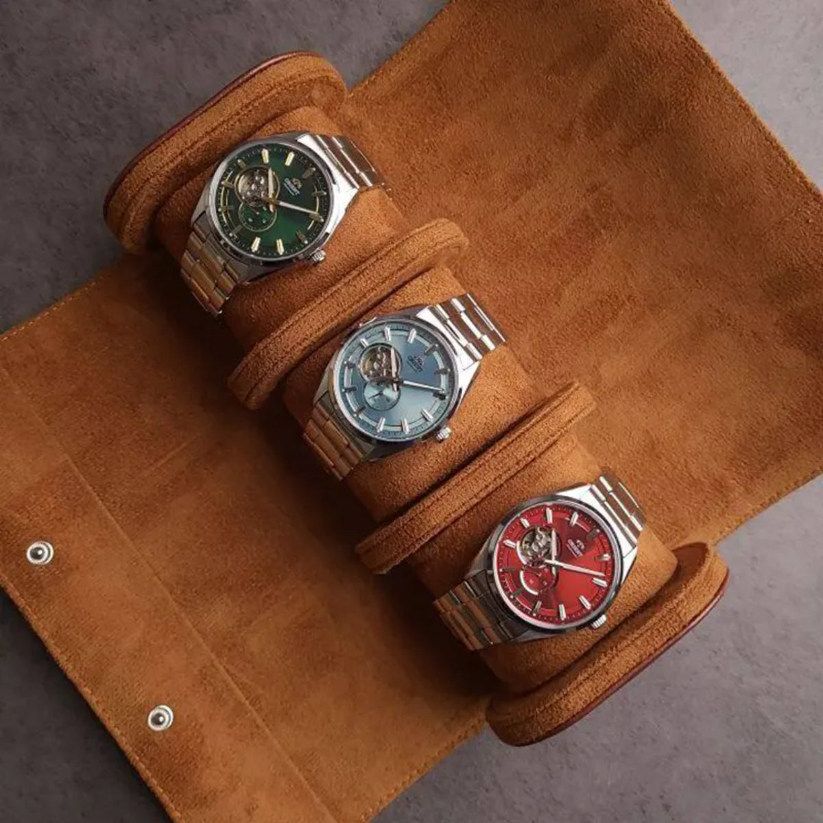 Three men’s automatic watches on a leather roll, featuring red open-heart dial