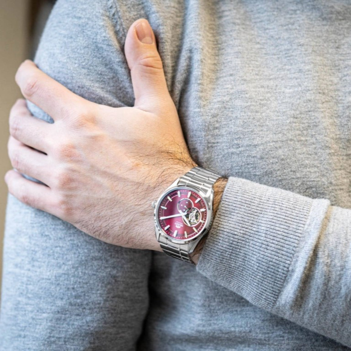 Men's automatic open-heart steel watch on wrist with red dial and metal link bracelet