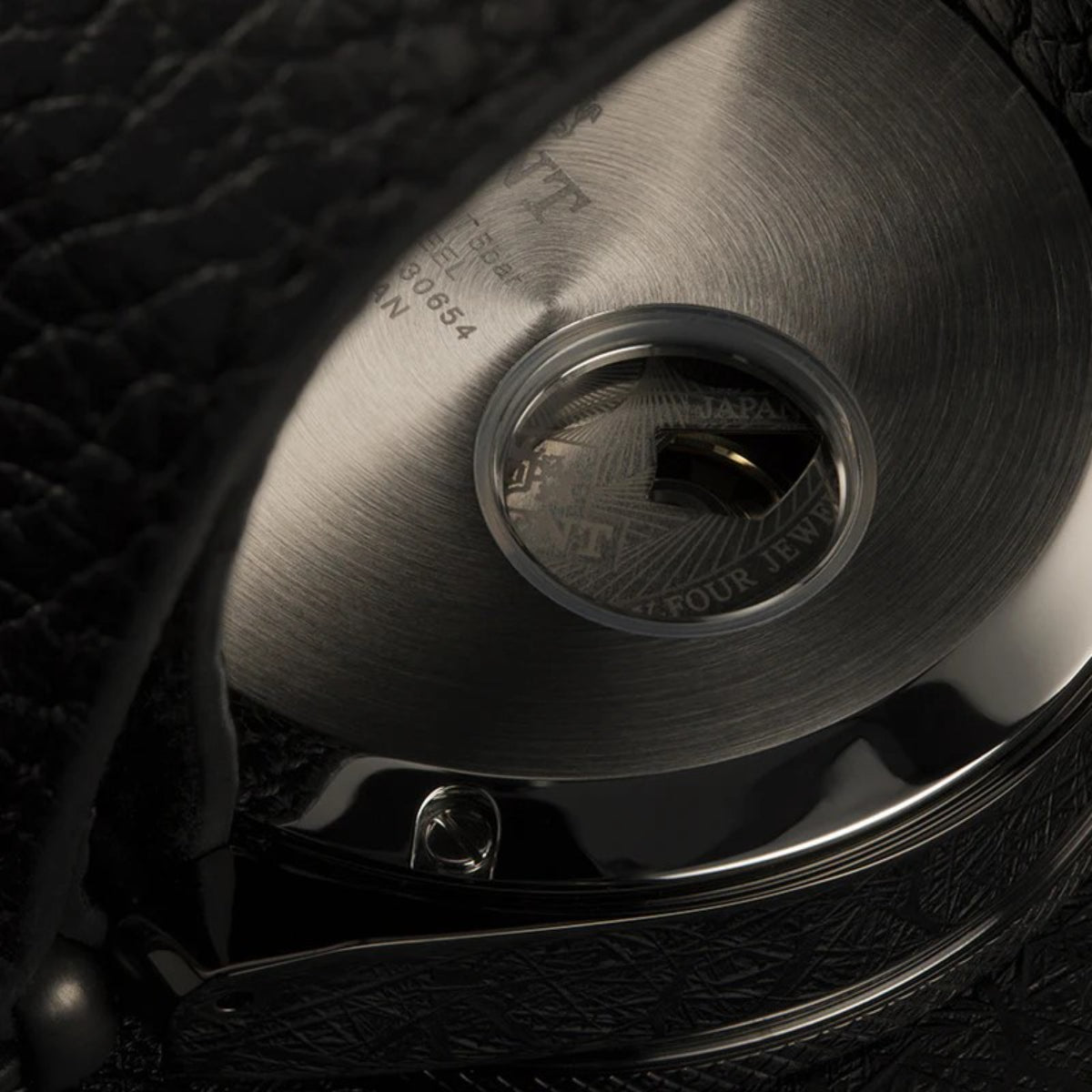 Men's automatic watch case with engraved text and crown against black leather