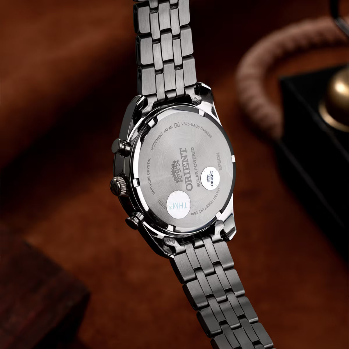 Solar-powered watch caseback on steel bracelet, engraved text and markings visible.