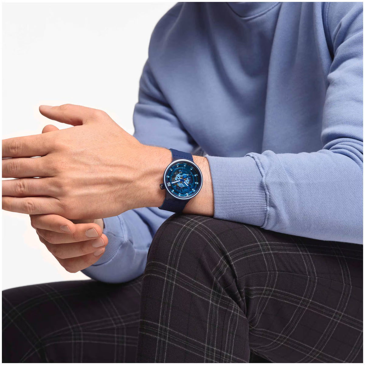 Blue silicone strap watch worn on wrist over light blue sweater cuff; round dial.