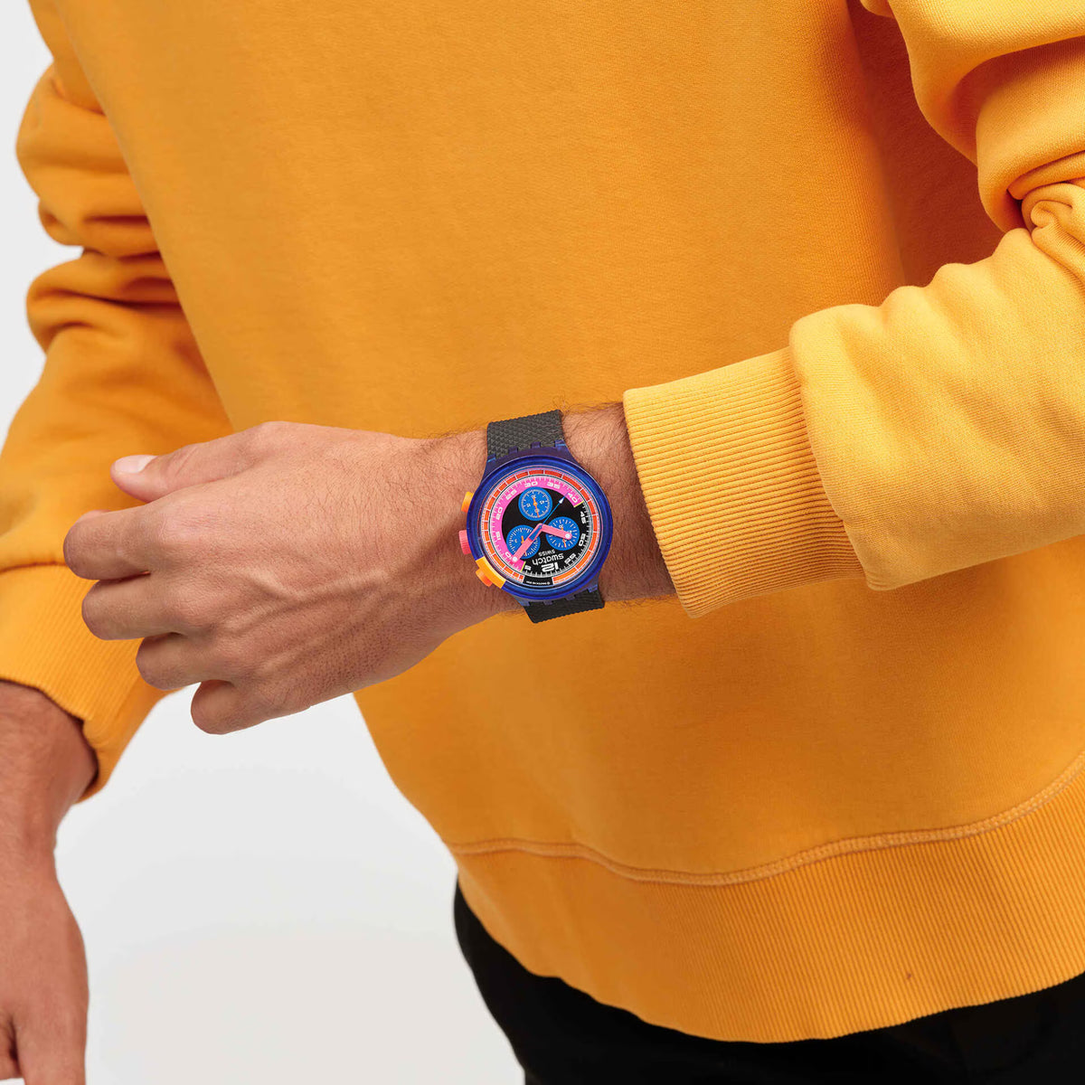 Men's sport watch on wrist with blue case, black strap, and neon multicolor chronograph dial