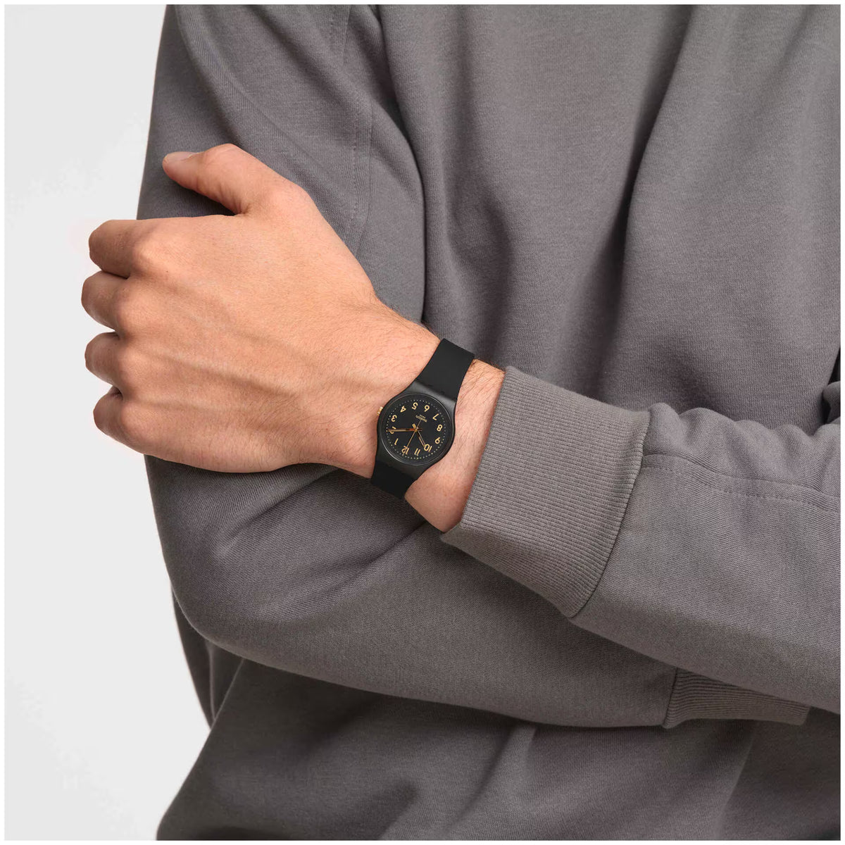 Swatch black dial watch on wrist, showing gold hands and black silicone band