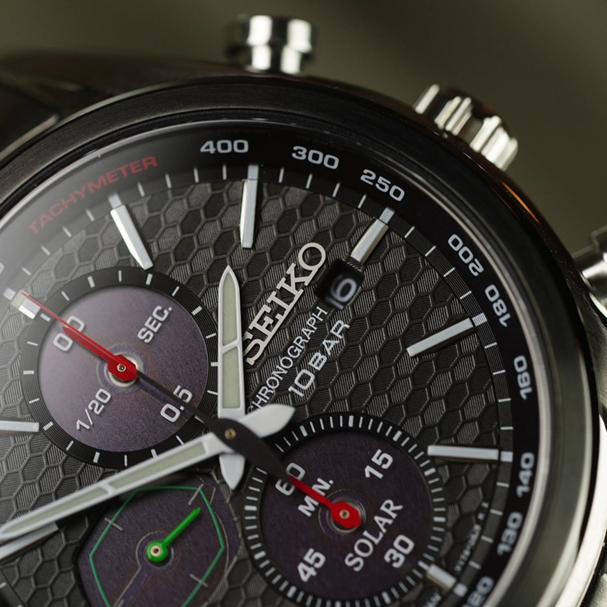 Solar chronograph close-up: black honeycomb dial with tachymeter and solar subdial