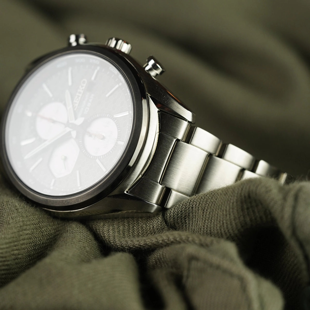 Solar chronograph wristwatch angled view with pale dial, black bezel, steel bracelet