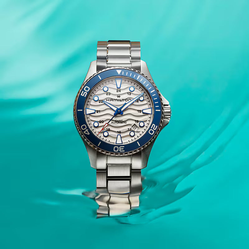 Hamilton Khaki Navy Scuba automatic watch with white wave pattern dial and blue bezel submerged in clear blue water