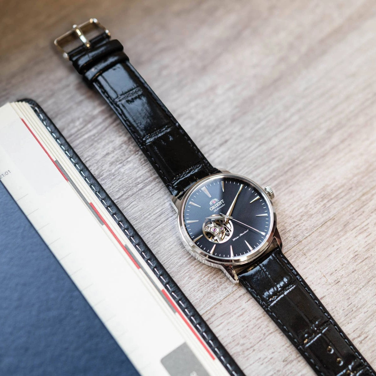 Orient automatic watch lying on wood with black leather strap and open-heart black dial