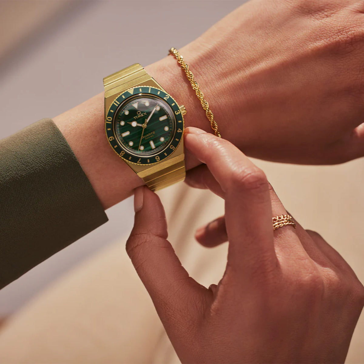 Gold-tone steel quartz watch with green dial and bezel on wrist