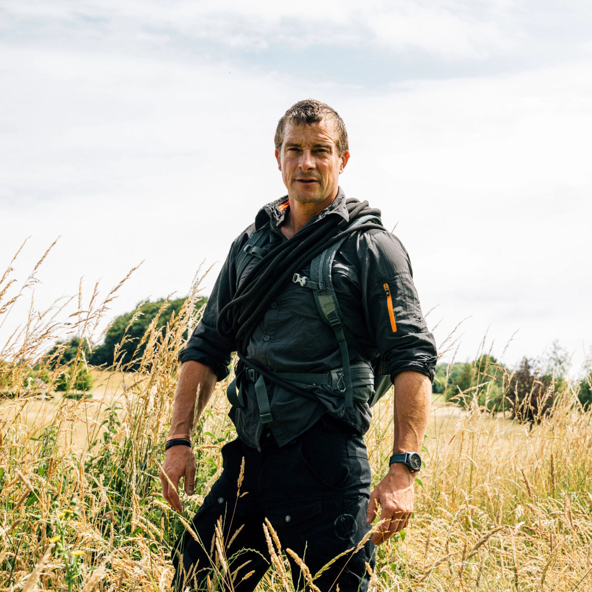 Bear Grylls standing in a tall grass field wearing the rugged Luminox Bear Grylls Survival XB.3716 field timepiece