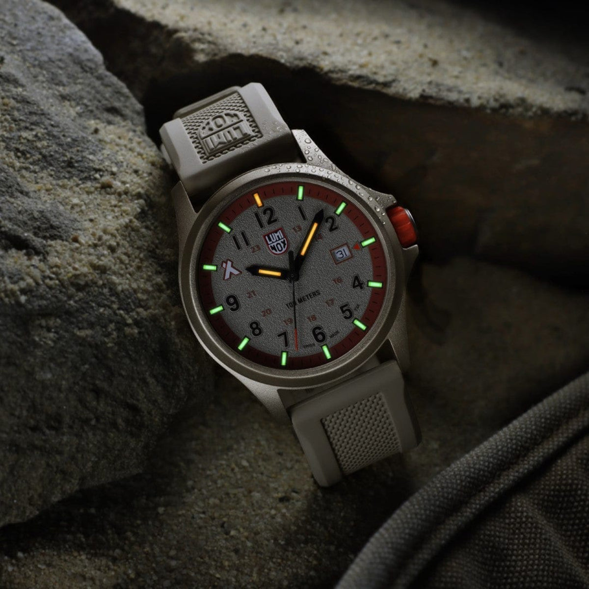 Illuminated self-powered tritium tubes glowing green and orange on the Luminox Bear Grylls Survival XB.3717 rested on dark rock