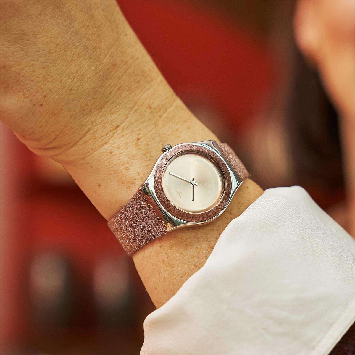 Rose-pink glitter synthetic strap watch worn on wrist with silver-tone round case