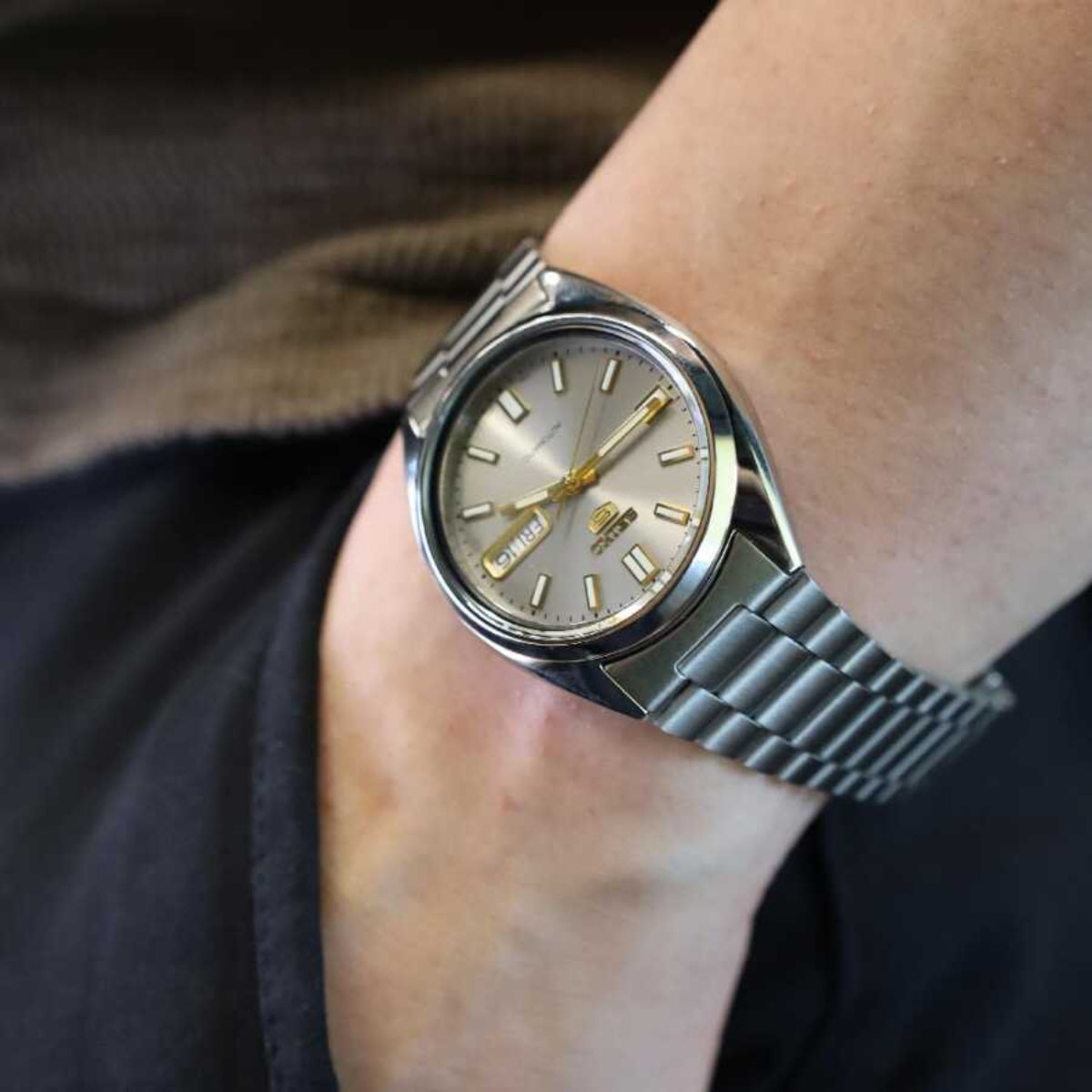 Seiko 5 automatic watch SNXS75K1 on wrist with grey dial, gold hands, and steel bracelet