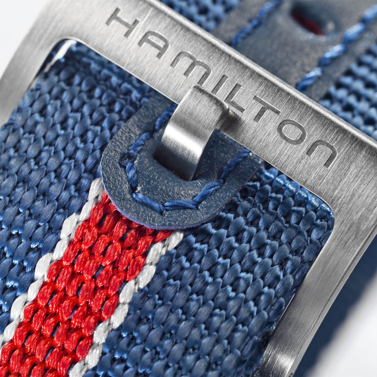 Close-up of an engraved stainless steel pin buckle on a Hamilton red, white, and blue striped textile watch strap