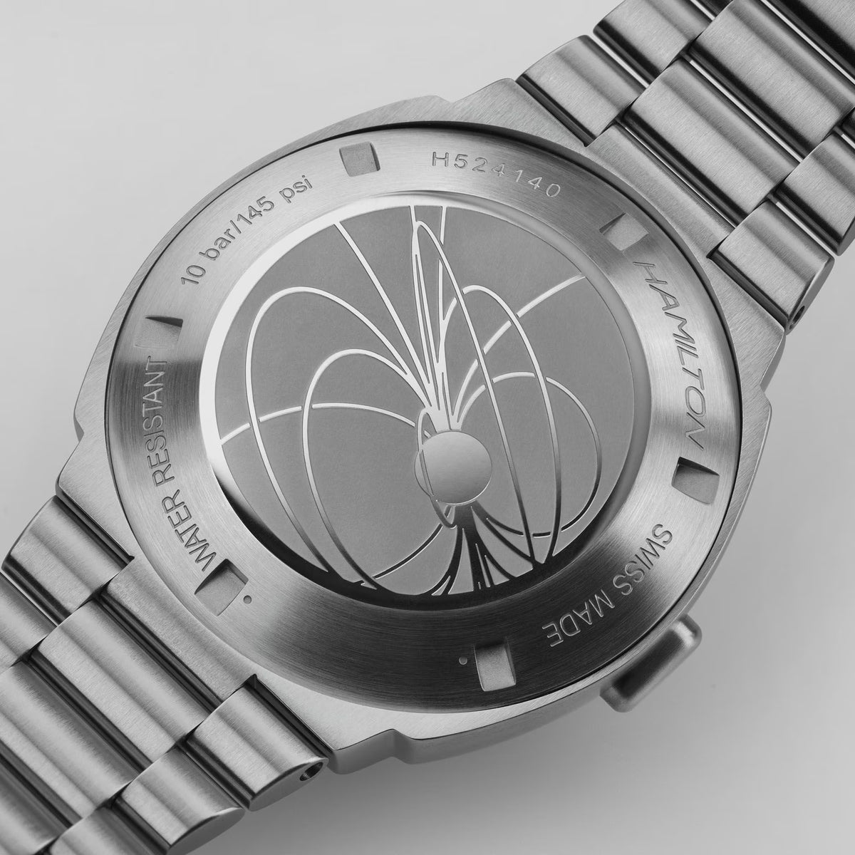 Close-up of a Hamilton PSR digital watch caseback, featuring an engraved magnetic field line design and stainless steel bracelet