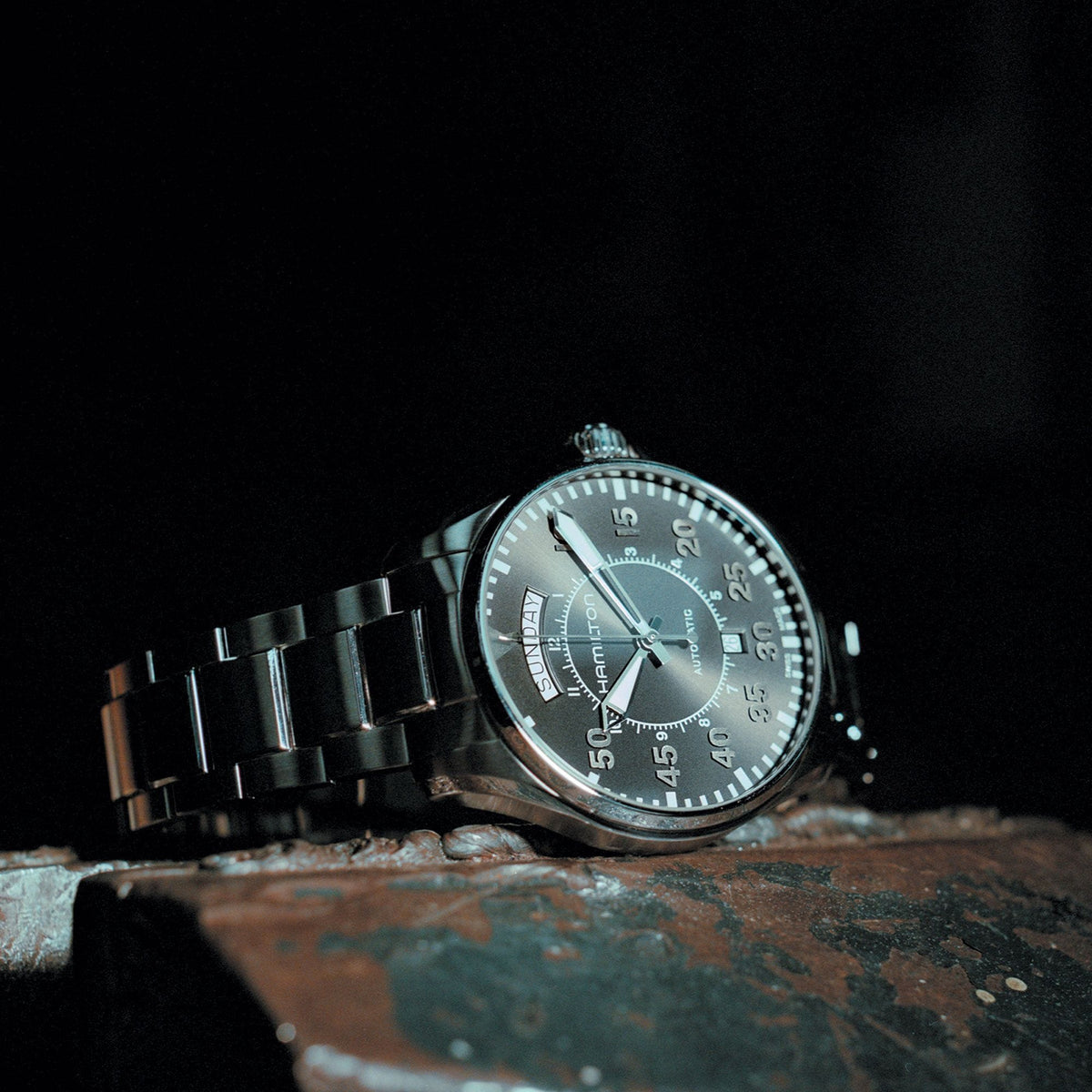 Low-light shot of the Hamilton Khaki Aviation H64615135 automatic timepiece resting on a metallic surface