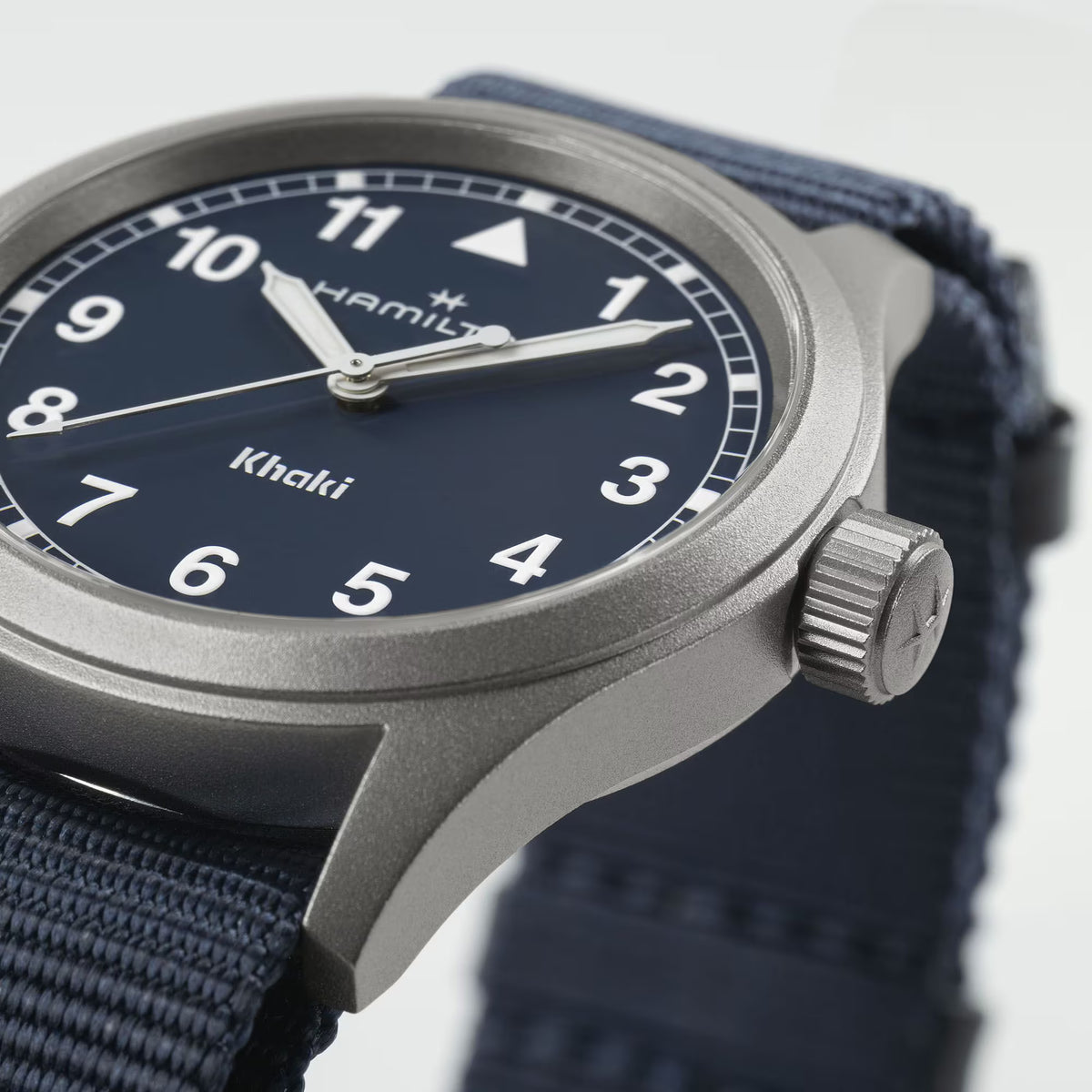 Blue dial watch close-up with gray case, ridged crown, and navy NATO strap
