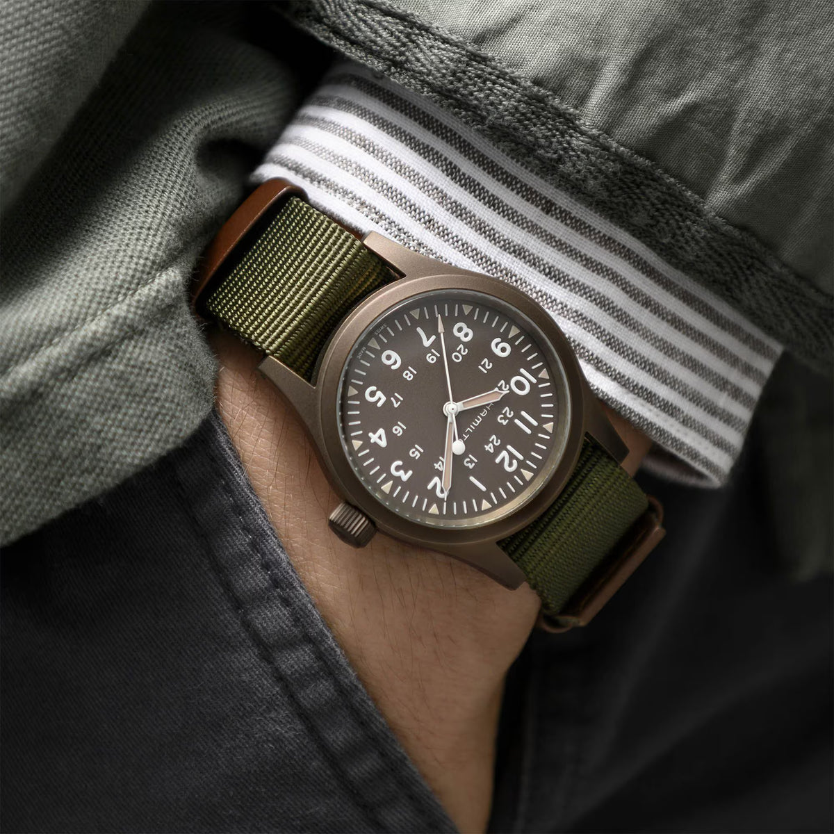 Men's mechanical field watch on wrist with olive NATO strap and green-toned dial