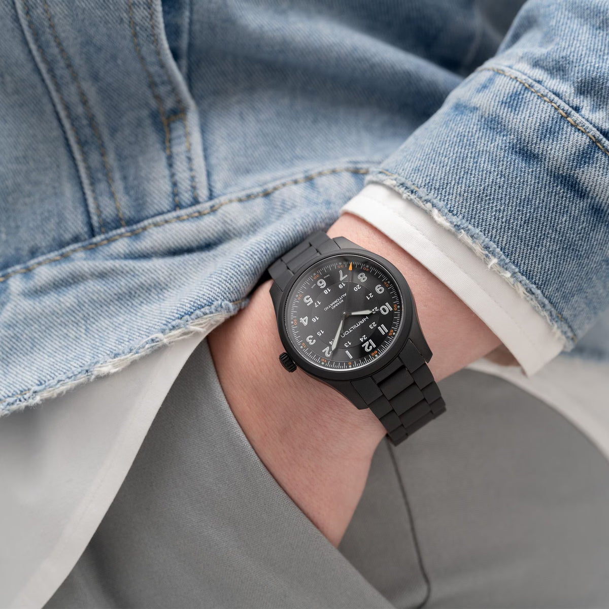 Black automatic wristwatch on a wrist with denim and white cuff