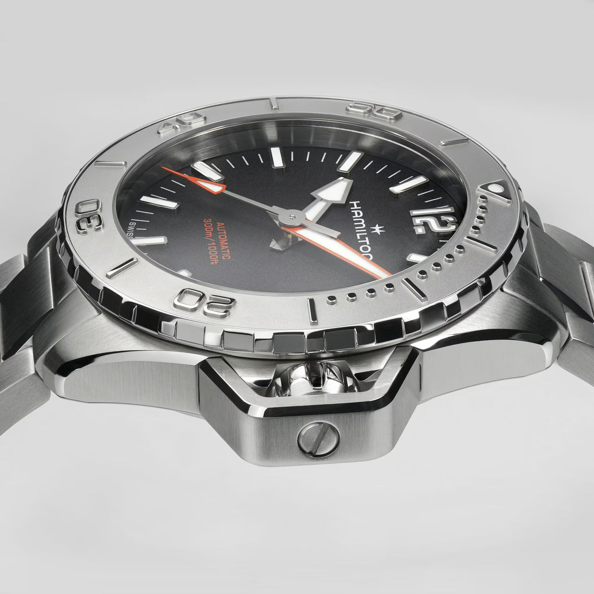 Close-up of steel watch case with black dial, orange hands, and bezel markers