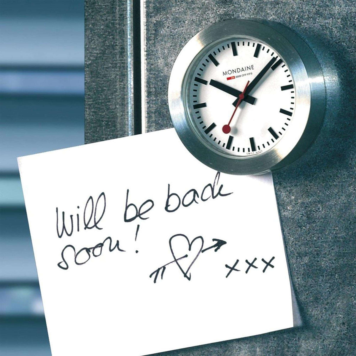 Mondaine Magnet Clock A660.30318.81SBB attached to a magnetic surface holding a handwritten note