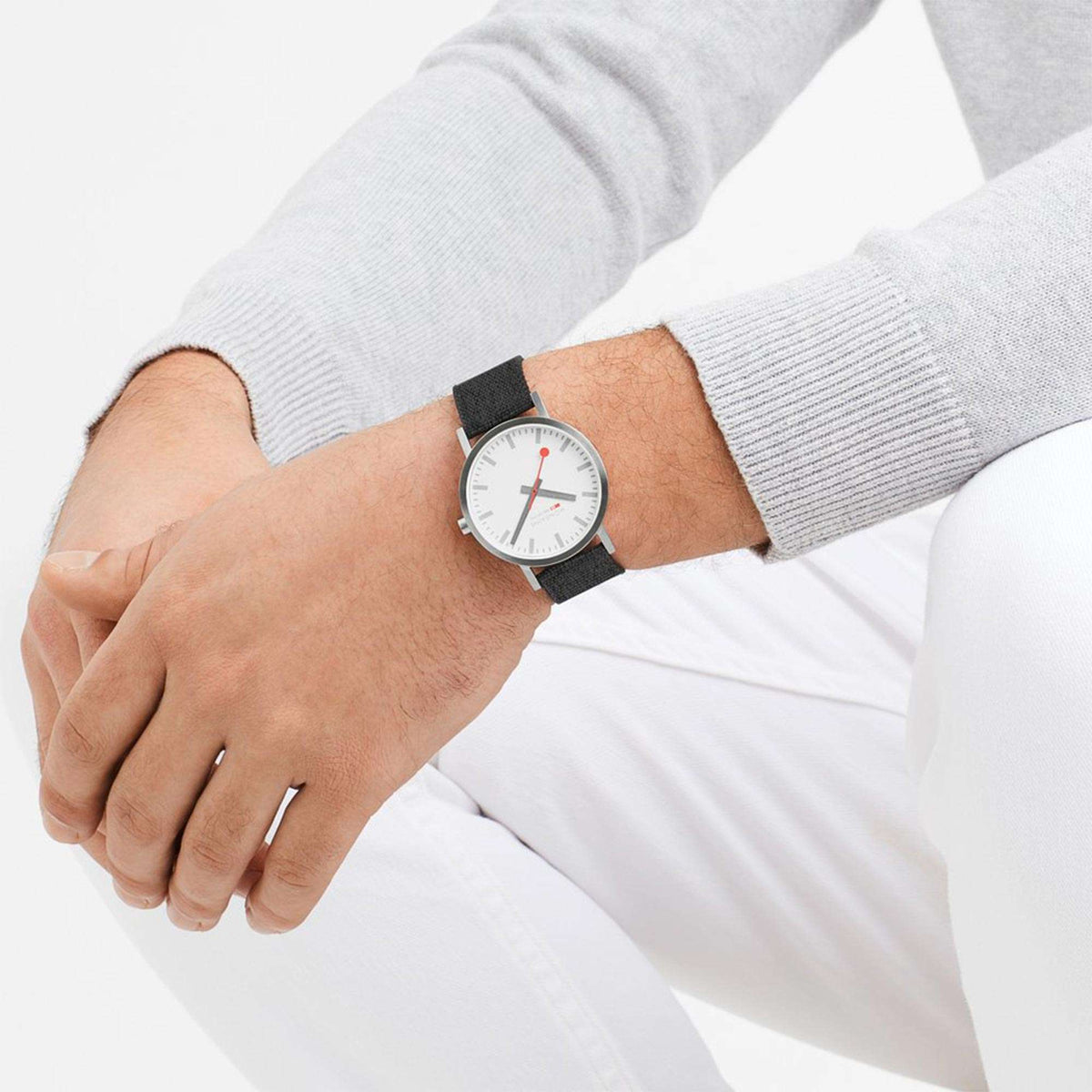Wristwatch on grey textile strap with white dial and red second hand on a man's arm