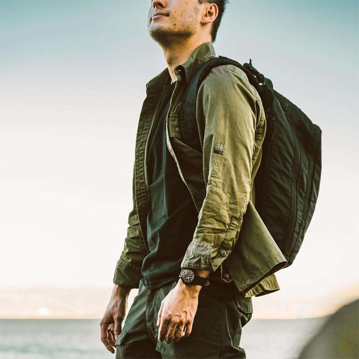 Men's black dial automatic watch on black leather strap worn with a field jacket.