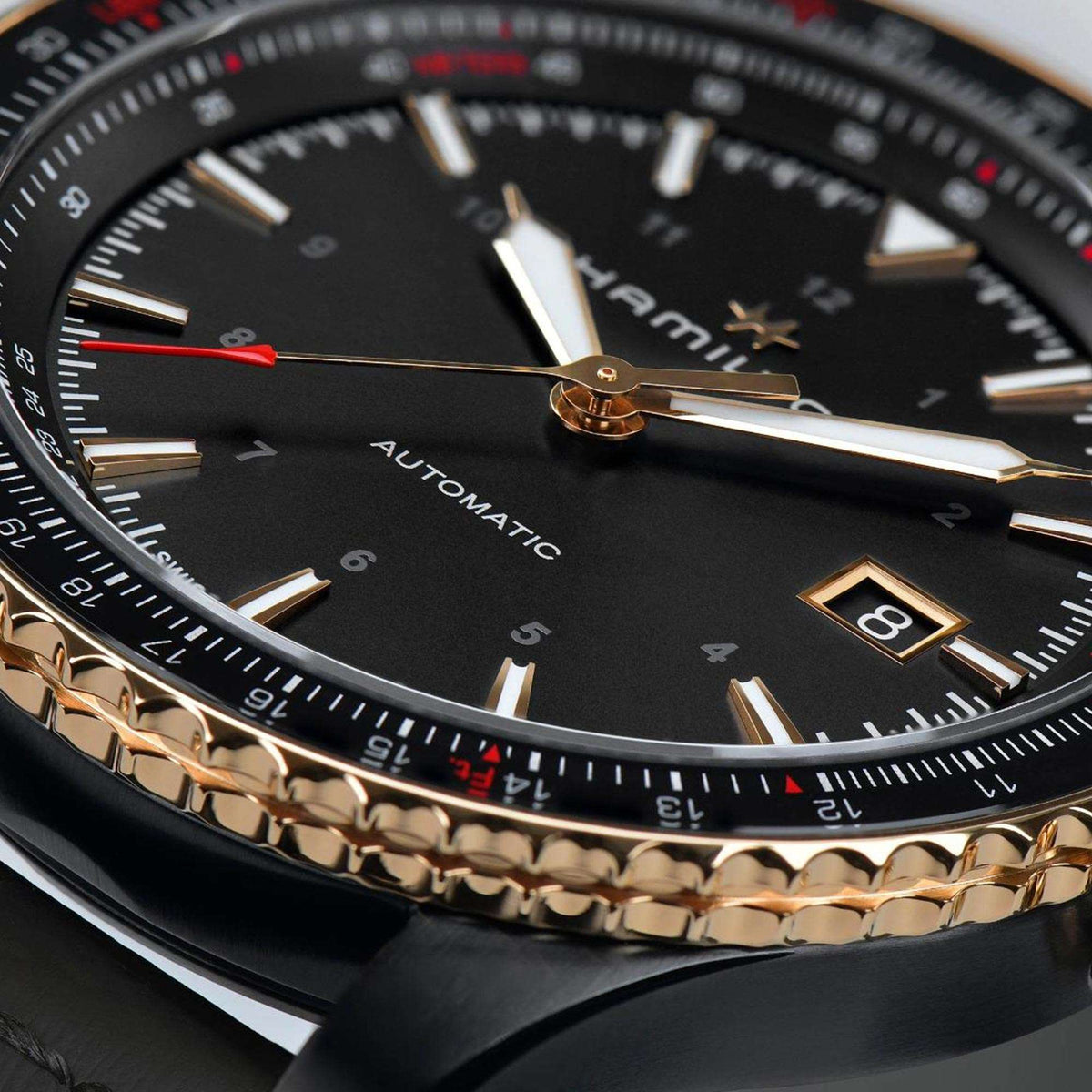 Men's automatic watch close-up: black dial, gold hands, red second hand, date marker.