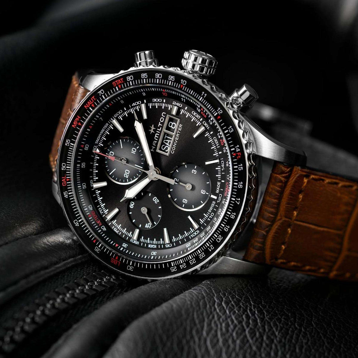 Men's chronograph watch with black dial and brown leather strap on dark surface